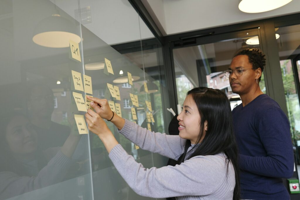 Homem e mulher interagem com quadro em ambiente empresarial, organizando post-its com jogos corporativos como ideias para o Setembro Amarelo nas empresas.