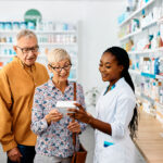 Farmacêutica afro-americana feliz aconselhando casal de idosos comprando vitaminas na farmácia, ação importante para o marketing farmacêutico.