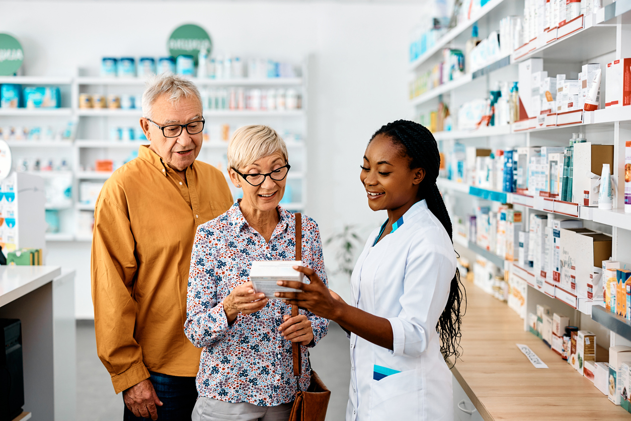 Farmacêutica afro-americana feliz aconselhando casal de idosos comprando vitaminas na farmácia, ação importante para o marketing farmacêutico.