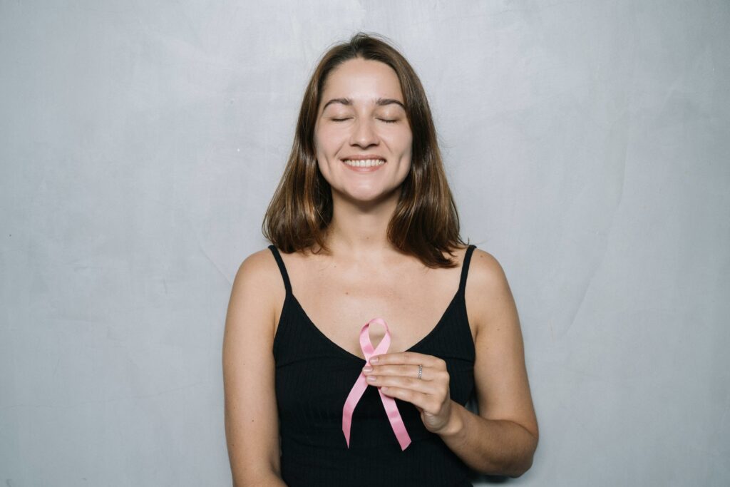 Mulher sorri e segura laço rosa, representando o utubro rosa: o que é e ideias de ações criativas para a conscientização nas empresas.