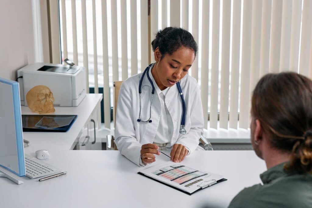 Jovem médica faz anotações sobre paciente em sua mesa, dentro de consultório, como exemplo de marketing farmacêutico para farmácias, distribuidoras e marketing farmacêutico para visitador médico.