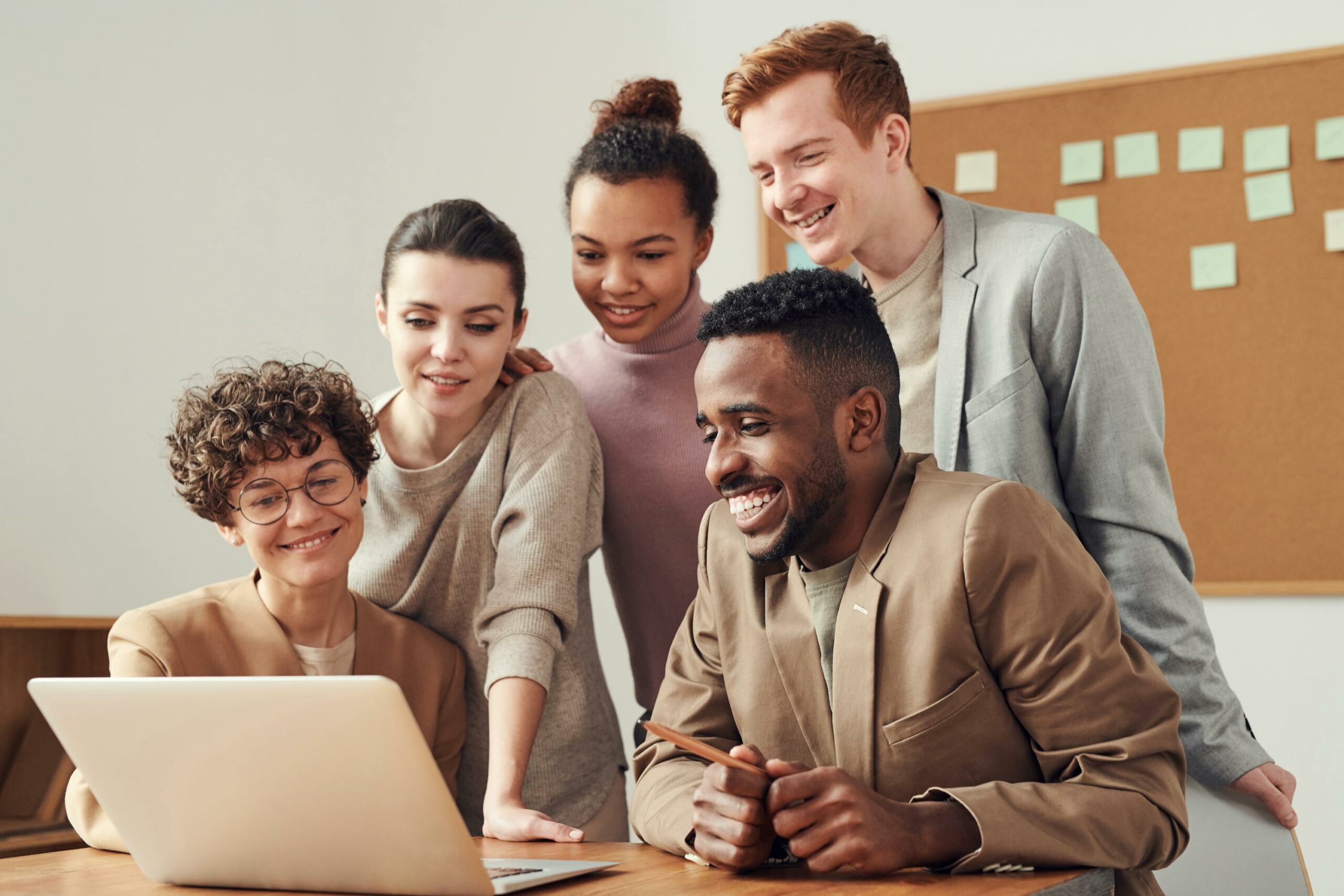 Equipe de 5 pessoas olha junta para tela de notebook, acessando jogos para treinamentos corporativos.