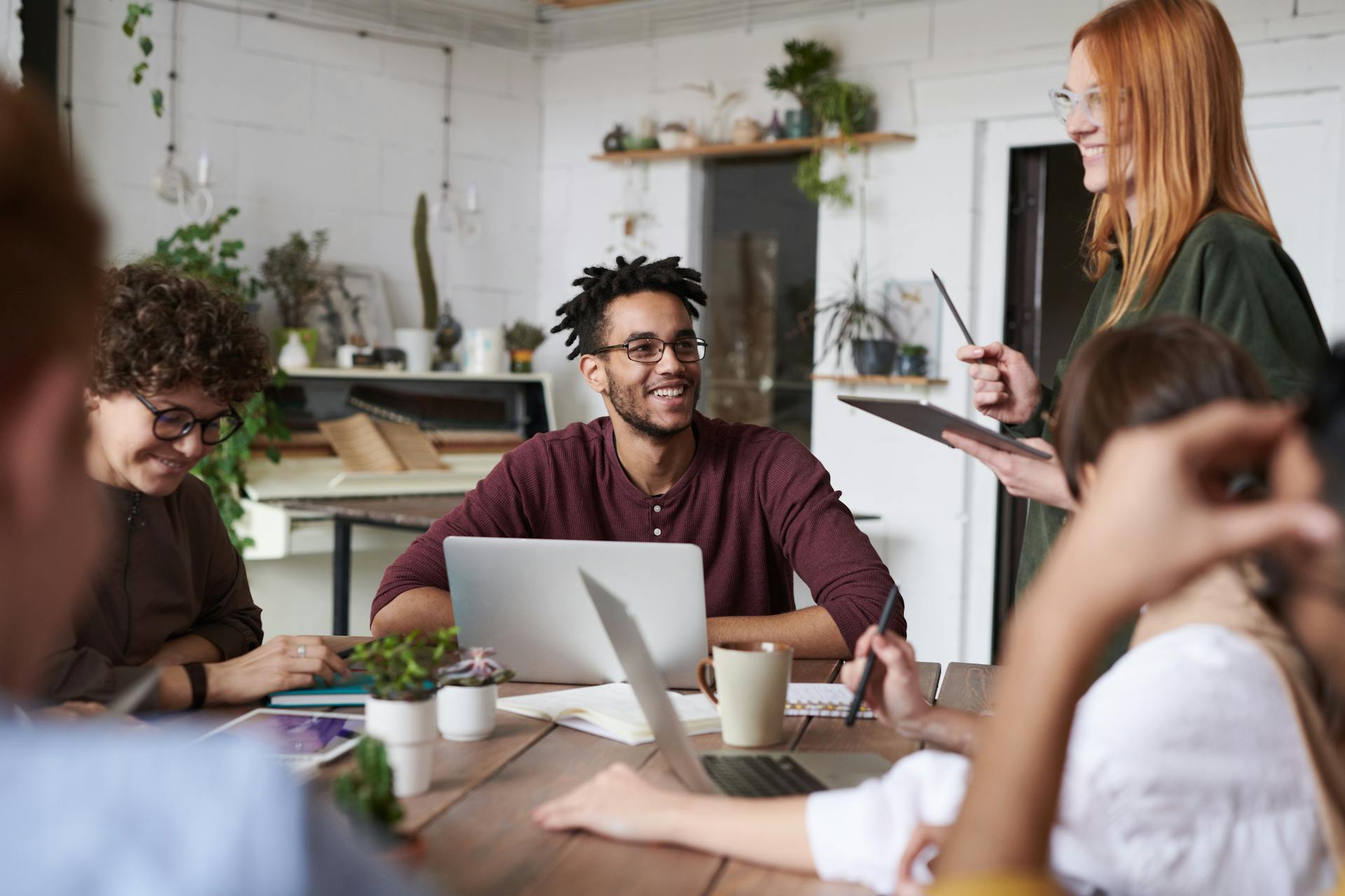 Equipe em torno de mesa com laptop, anotações, xícaras e tablets, conversando e sorrindo, representando as plataformas de treinamentos personalizadas PlayerUm.