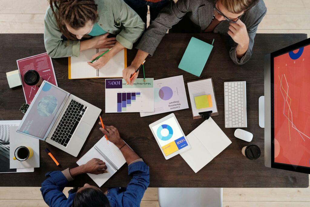 Time de Marketing trabalhando junto em mesa com documentos que mostram dados e planos de ação representam ideias de ações de endomarketing para o Novembro Azul, como brindes e campanhas internas.