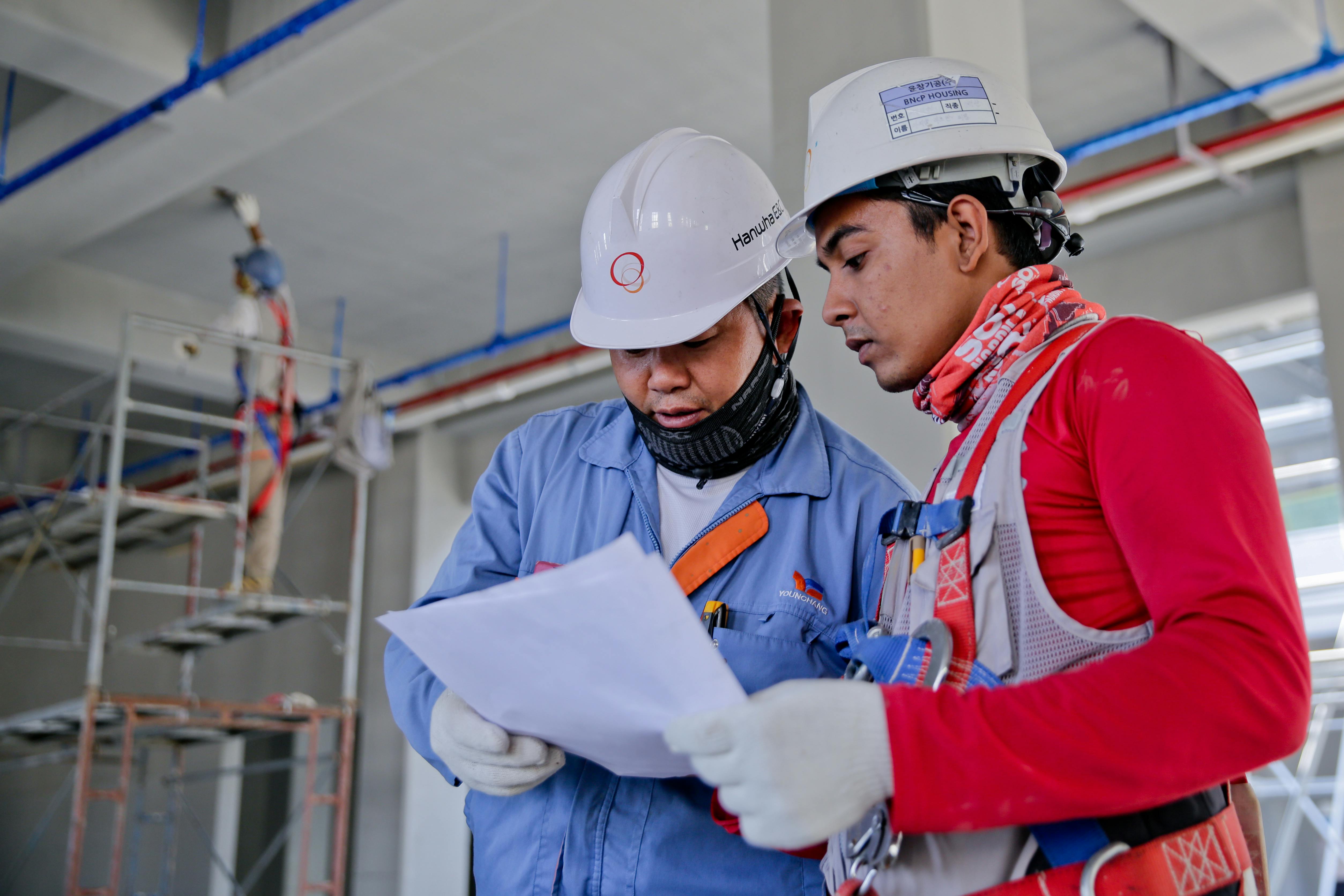 dois homens equipados com EPI's lendo um manual de trabalho, representando a segurança no trabalho