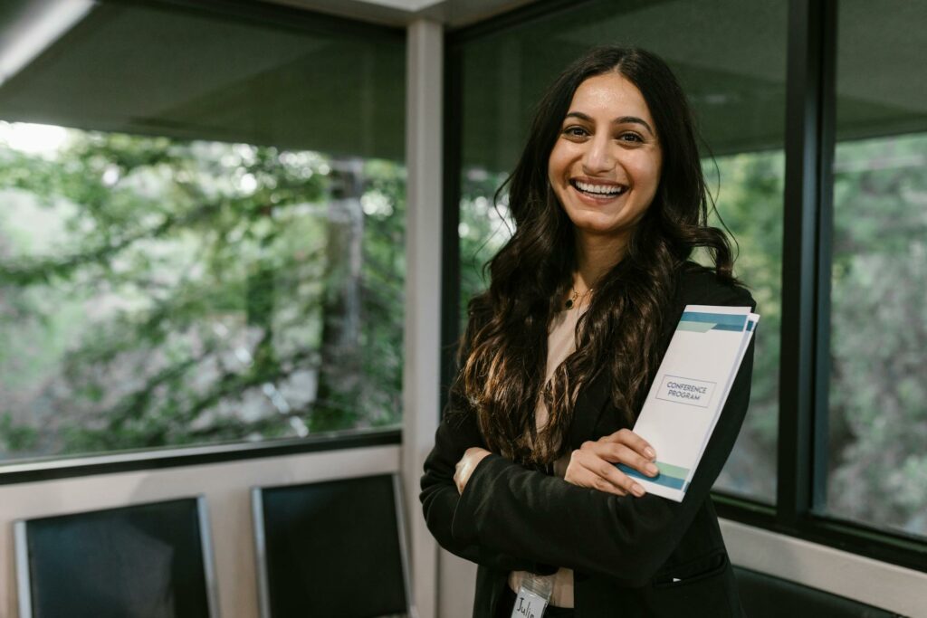 Uma mulher sorridente e confiante segura o guia de um programa de conferências, pronta para aproveitar ao máximo um evento corporativo B2B. Inspire-se na alegria e prepare-se para ações para eventos corporativos eficazes!