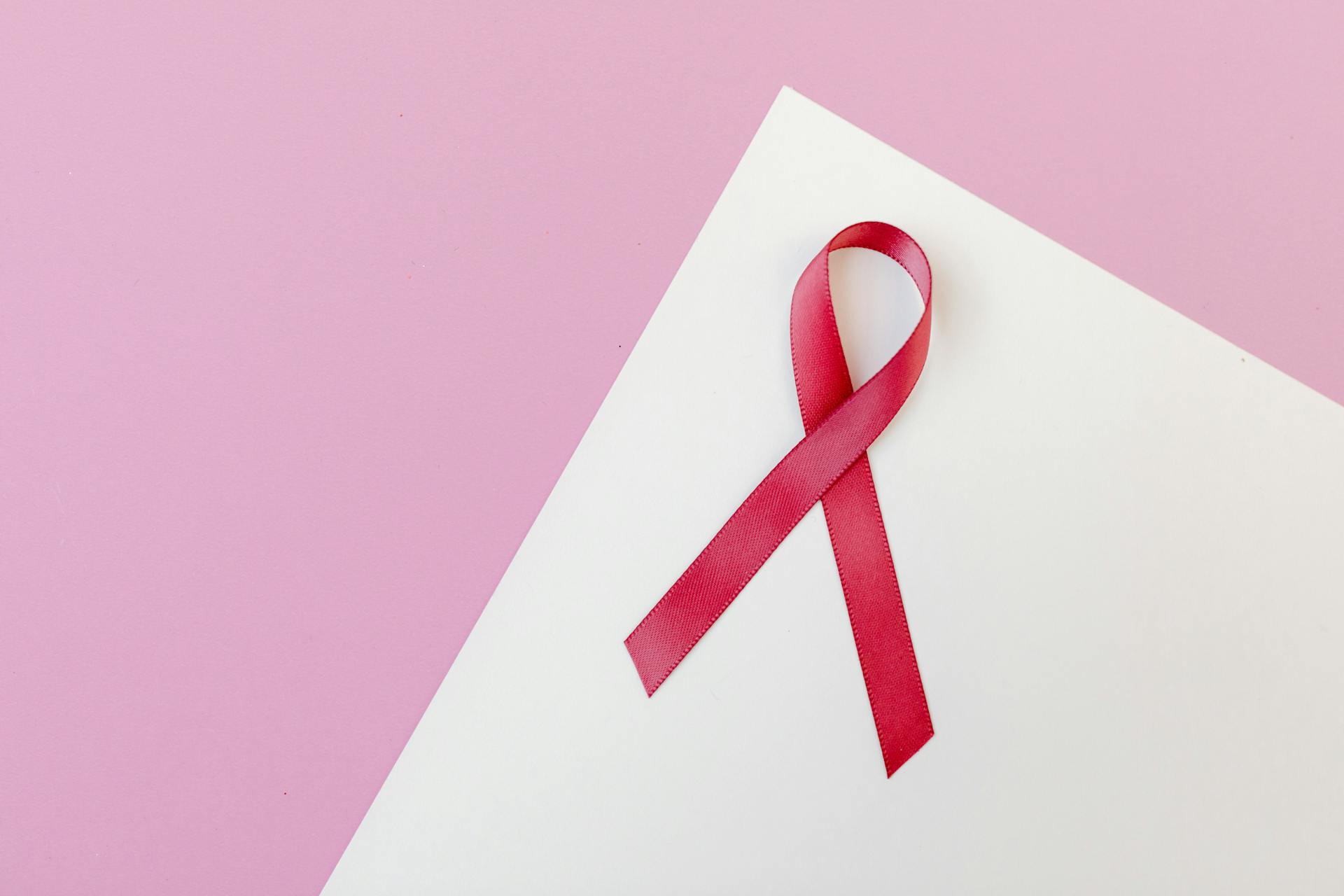 Fita vermelha sobreposta a papel ofício branco e fundo rosado representa o Junho Vermelho campanhas para empresas.