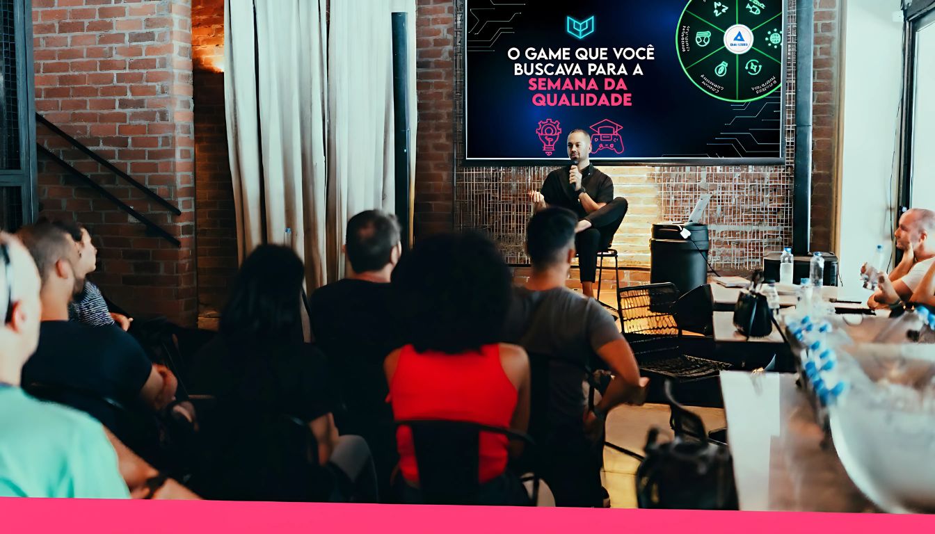 um homem sentado de frente para um público apresentando ideias de gamificação para a semana da qualidade